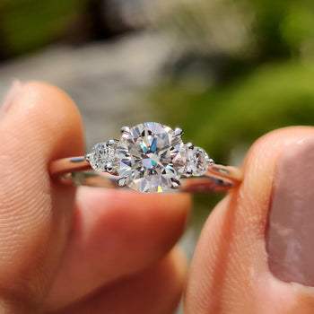 Simple three-stone round engagement ring in white gold with moissanite center.