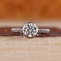 Round cut diamond ring with bezel setting in white gold.