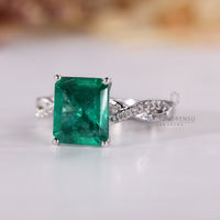 Twisted pave ring holding green emerald with round diamond details.