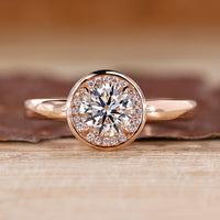 Round cut diamond ring with bezel set and halo diamond design in rose gold.