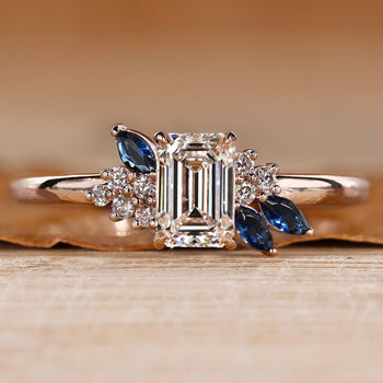 Asymmetrical cluster ring with an emerald center stone.