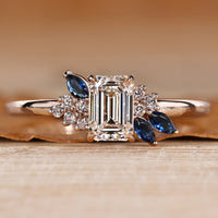 Asymmetrical cluster ring with an emerald center stone.
