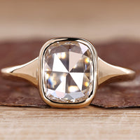 Solitaire engagement ring with cushion rose cut diamond and bezel setting.