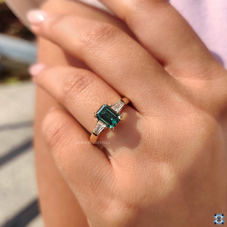 Buy Engagement Ring with a breathtaking Emerald Cut Moissanite and delicate side stones.