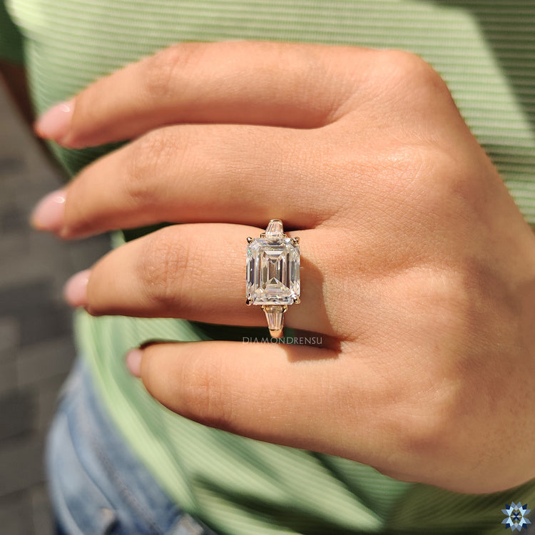 Side stone engagement ring with an emerald cut moissanite and tapered baguette diamonds.