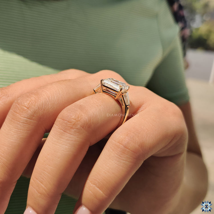Yellow gold engagement ring featuring emerald cut moissanite and tapered baguette side stones.