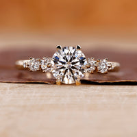 Side Stone Engagement Ring with round cut diamonds in a six claw prong setting.