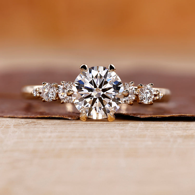 Side Stone Engagement Ring with round cut diamonds in a six claw prong setting.