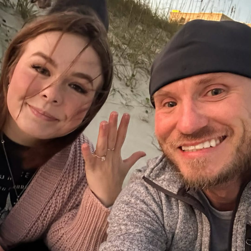 Smiling couple celebrating their engagement outdoors with a diamond ring Smiling couple celebrating their engagement outdoors with a diamond ring