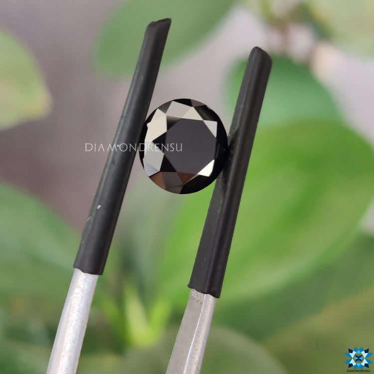 Round cut moissanite beside black loose moissanite stone.