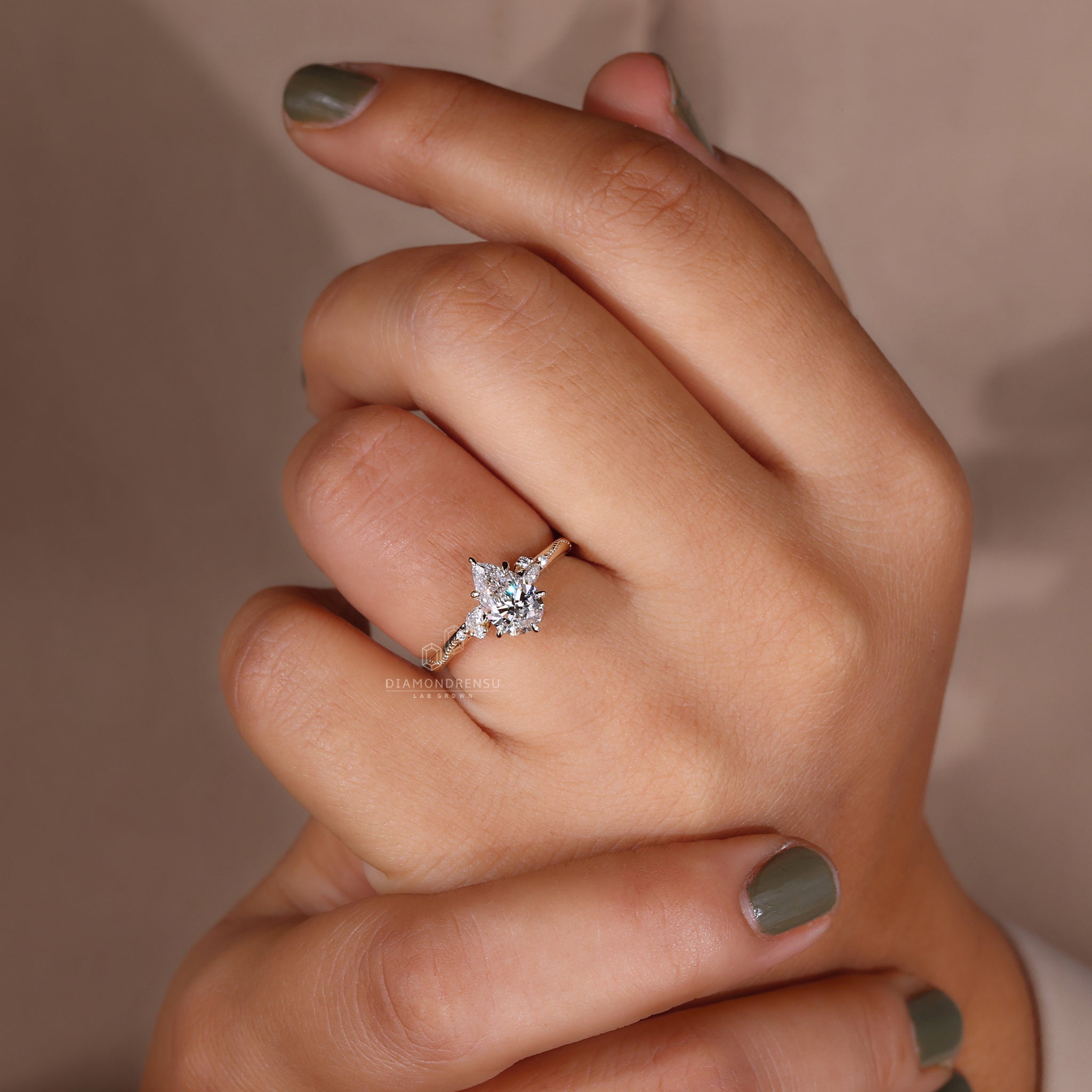 Pear cut diamond ring with claw prongs and round and marquise side stones on a model.