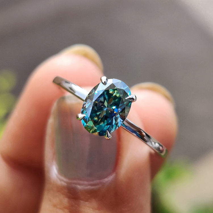 Oval moissanite engagement ring with cyan blue center stone.
