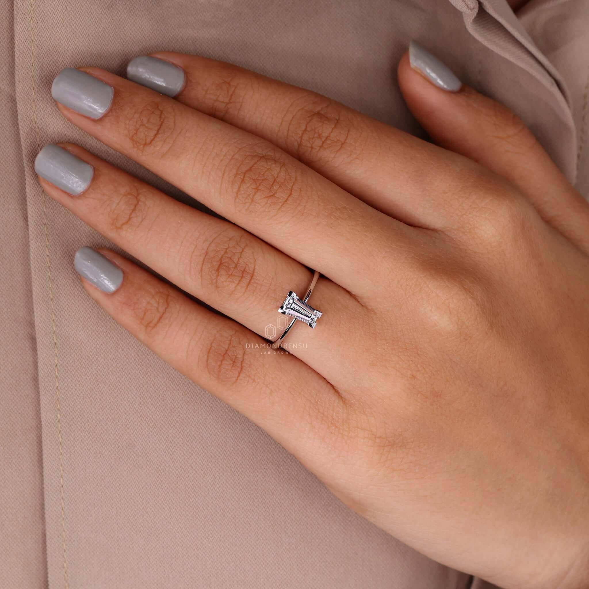 Model's finger with a solitaire diamond ring accented by baguette diamonds