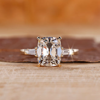 Old mine cushion cut diamond ring with tapered baguette side stones, offering a unique design.
