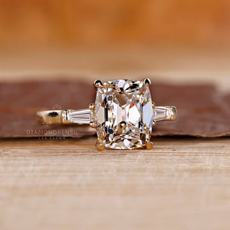 3-stone engagement ring with a cushion cut diamond center and tapered baguette side stones.
