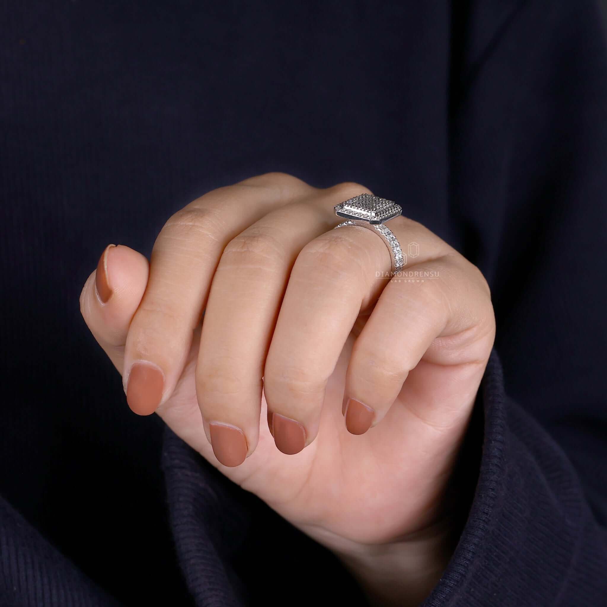 man maA close-up shot of a man kneeling down, holding an open jewelry box with a dazzling round diamond engagement ring in a cluster setting. The background is blurred.