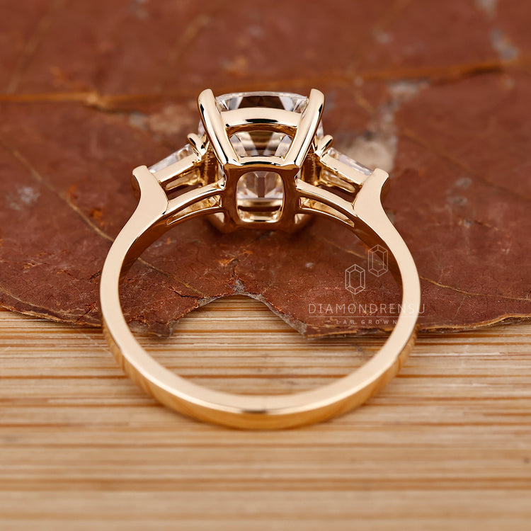 Unique engagement ring with a cushion cut diamond and tapered baguette side stones, set in yellow gold.
