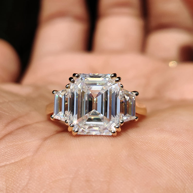 Three stone engagement ring with a stunning emerald cut moissanite center.
