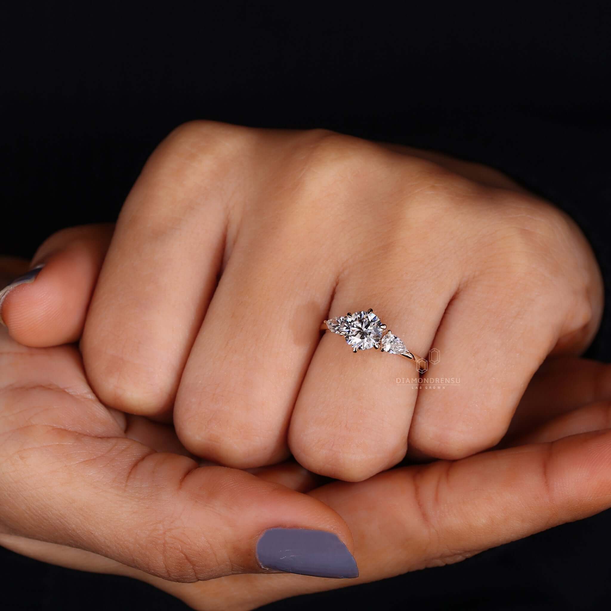 Hand wearing a round diamond ring with pear side stones, emphasizing its unique charm and brilliance.