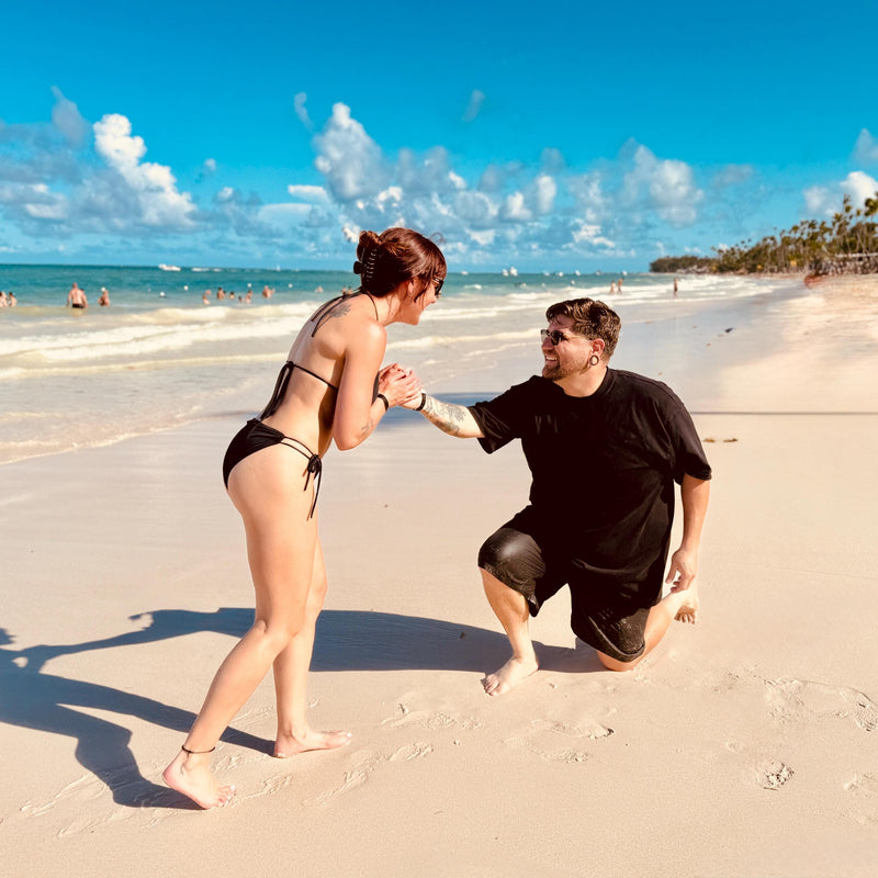 Man kneeling on a sandy beach proposing to a woman
