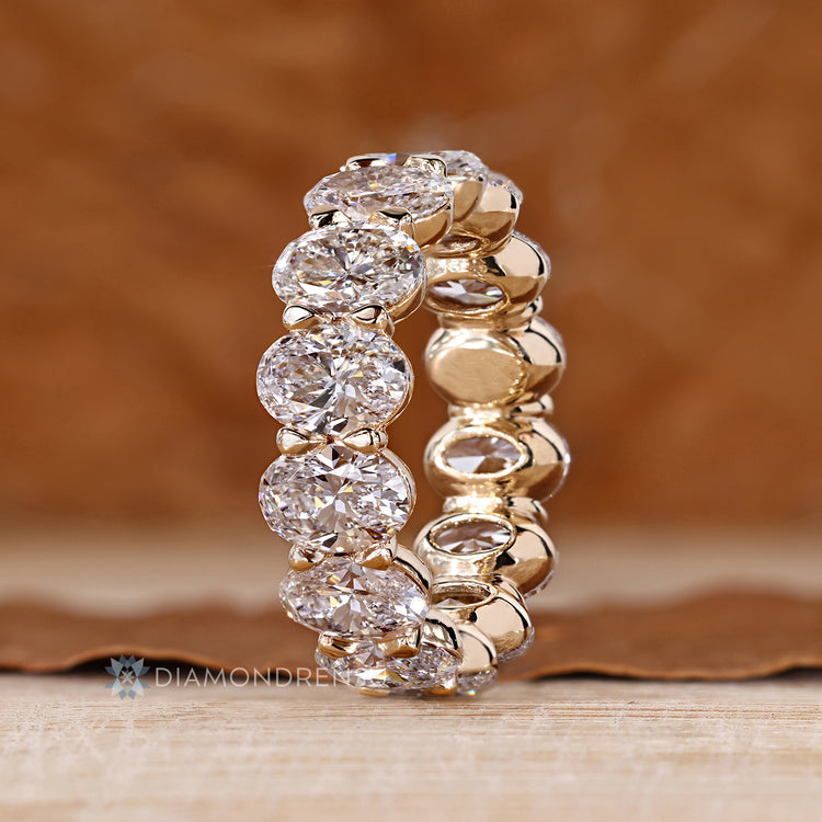 Oval diamond wedding band with bezel basket and shared prong details.