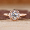 Round cut diamond ring with bezel set and halo diamond design in rose gold.

