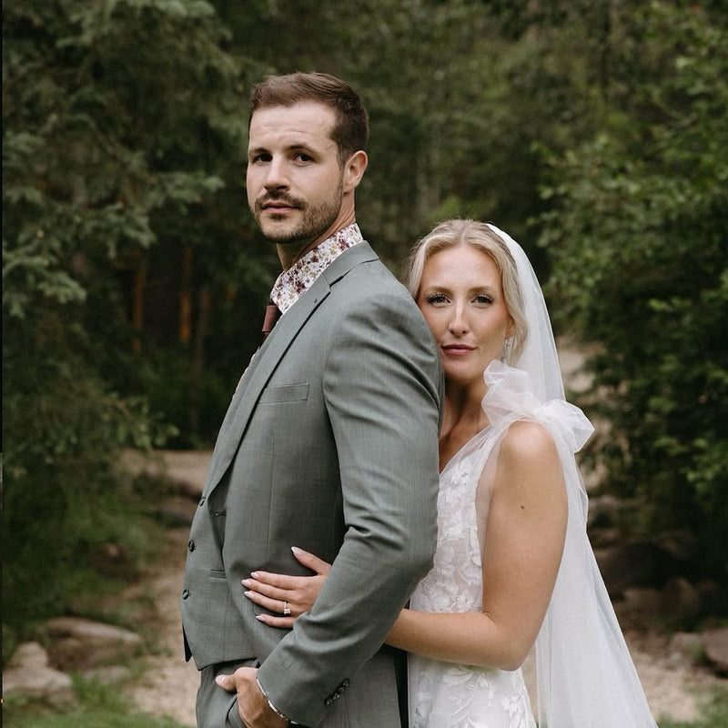 Bride in lace wedding dress embracing groom in grey tweed suit