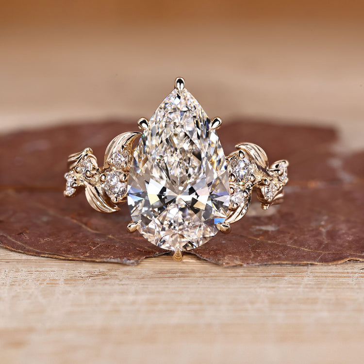 Pear cut engagement ring with nature inspired design and round side stones.
