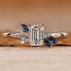 Asymmetrical cluster ring with an emerald center stone.