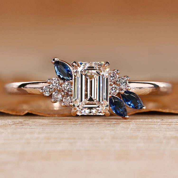 Asymmetrical cluster ring with an emerald center stone.