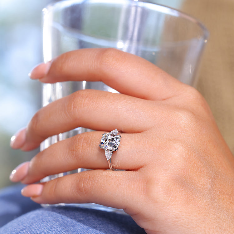 Cushion old mine diamond with pear side stones and double claw prongs.