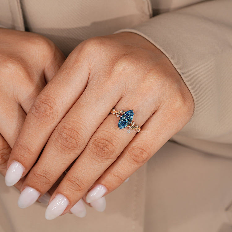 Blue marquise engagement ring with a tulip setting and six leaf style prongs.