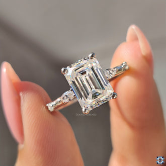 White gold engagement ring featuring an emerald cut moissanite stone.
