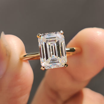 Hidden halo emerald cut engagement ring on a white display.
