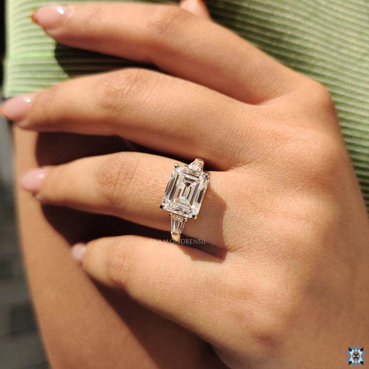 Custom engagement ring featuring emerald cut moissanite in a unique east to west setting.

