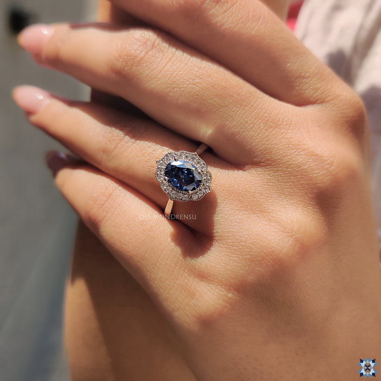 Diamondrensu ring with a blue Oval Cut Moissanite set in a vintage halo design.
