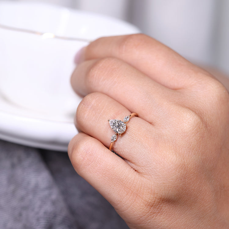 Marquise side diamond ring featuring pear center diamond in prong setting.
