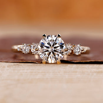 Side Stone Engagement Ring with round cut diamonds in a six claw prong setting.
