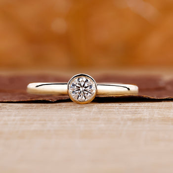 A yellow gold bezel set diamond ring with a round cut diamond center.
