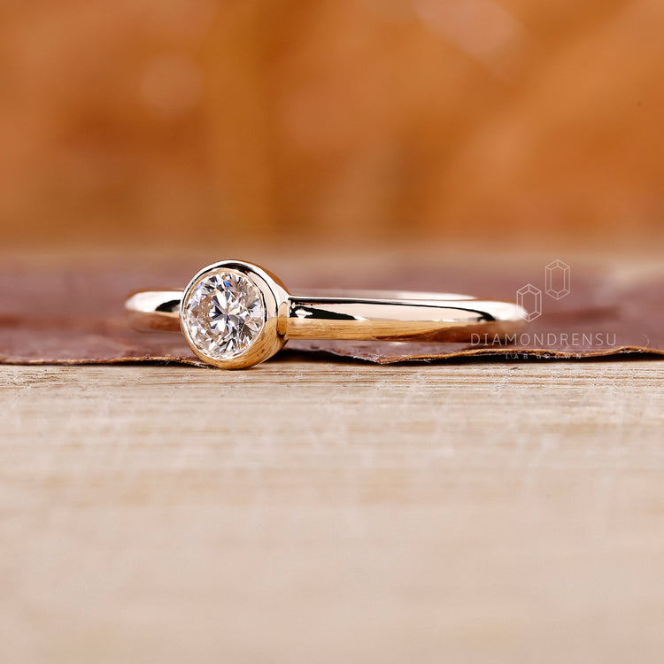 A solitaire setting in a yellow gold bezel set diamond ring.
