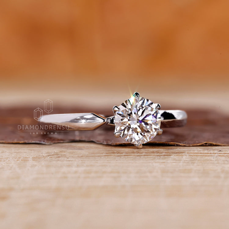 Pinched shank ring showcasing round diamond solitaire in white gold.
