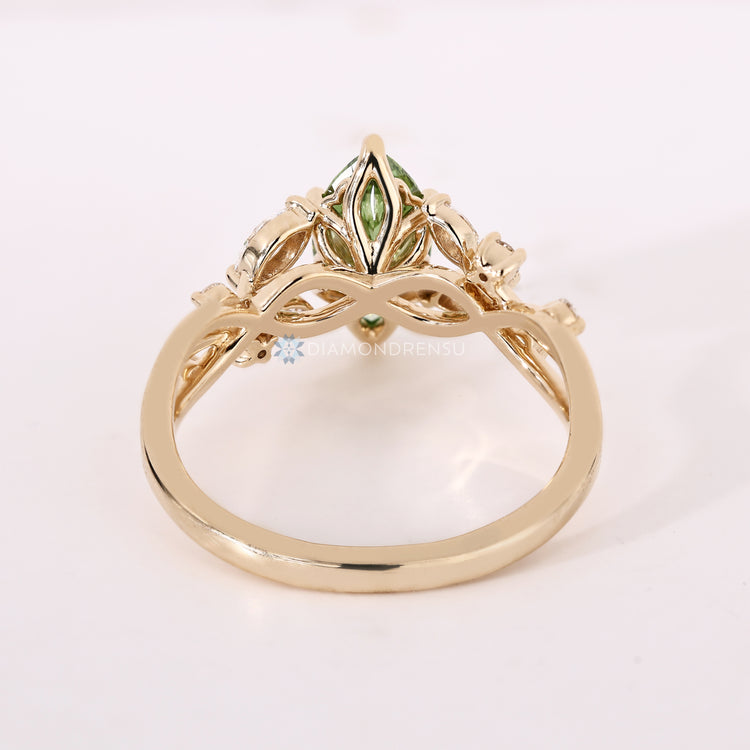 Green marquise diamond ring with round and marquise side stones and a six prong setting.