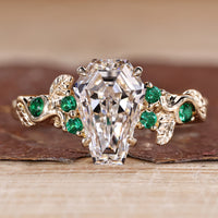 Coffin cut engagement ring with green emerald and round side stones.