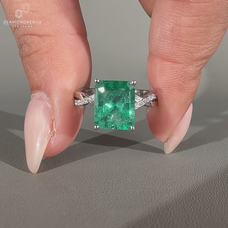 Green emerald ring featuring round diamond pave in white gold.
