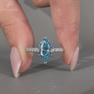 Blue diamond ring featuring marquise cut stone and round cut pave band.
