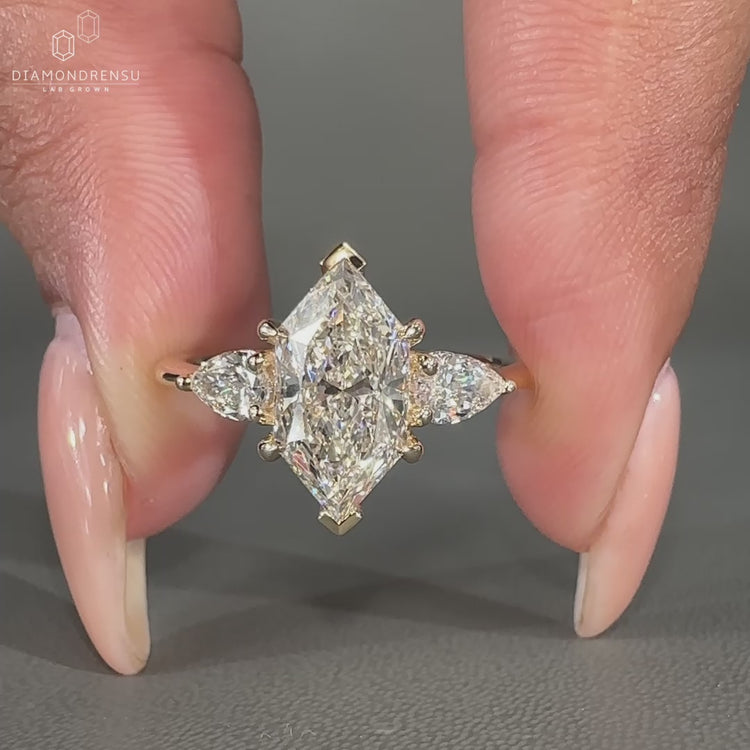 Three stone engagement ring with two pear cut side stones, tapered shank band, and yellow gold engagement ring.
