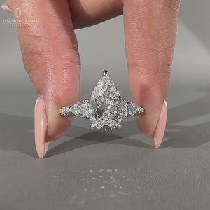 Three stone ring featuring pear cut diamond and round side stones.
