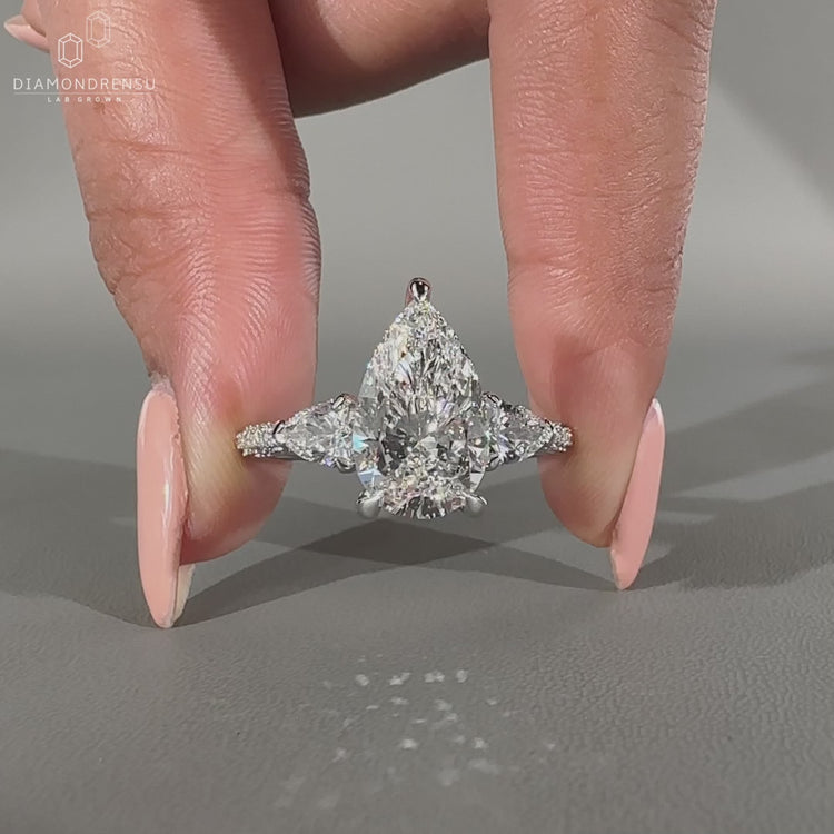 Three stone ring featuring pear cut diamond and round side stones.
