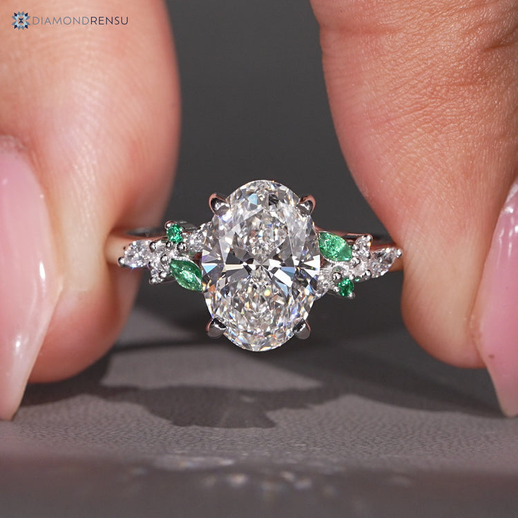 Oval engagement ring with green emerald side stones.