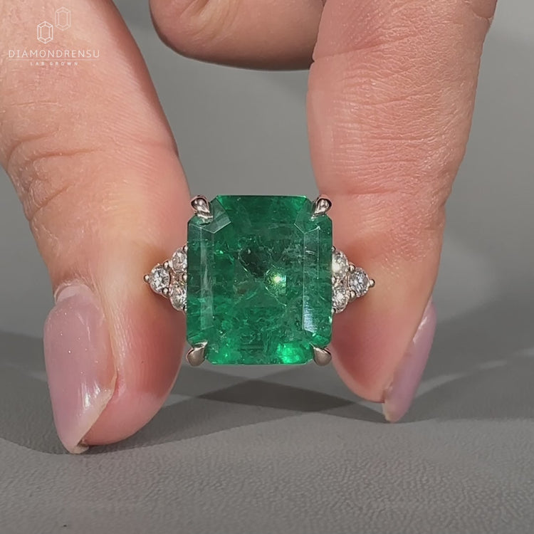 Green emerald gemstone ring with round side stones.
